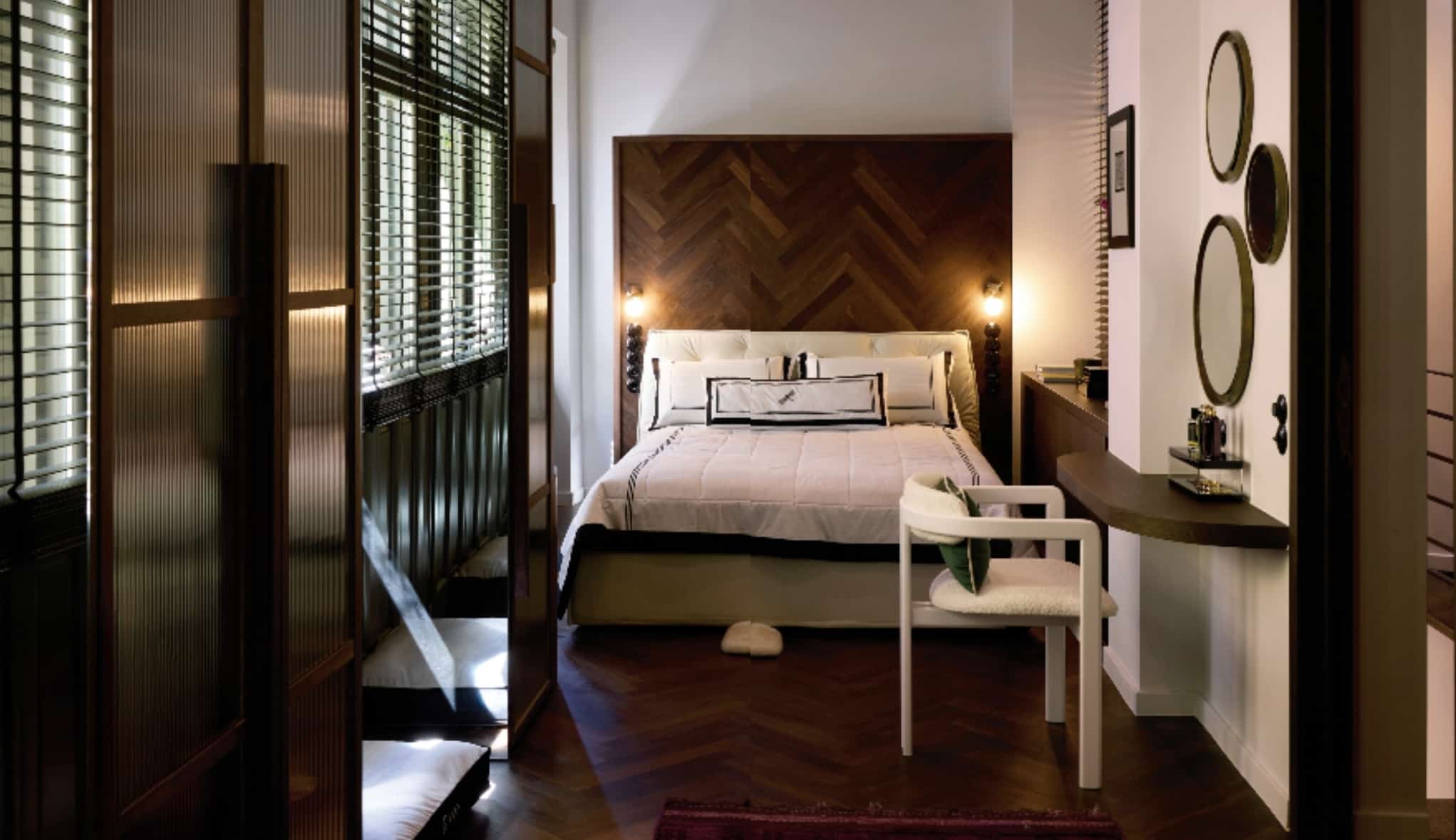 Στο master bedroom, εντυπωσιάζουν τα ξύλινα στόρια σε αποικιακό στιλ. Ανάμεσα στα παράθυρα υπάρχουν μικρές ντουλάπες με καθρέφτη στο πλάι τους, όπου καθρεφτίζονται τα στόρια δημιουργώντας την αίσθηση της τεράστιας τζαμαρίας. Πίσω από το κρεβάτι, ένα ξύλινο πάνελ διορθώνει το παράγωνο του δωματίου και δημιουργεί έναν ανοιχτό αποθηκευτικό χώρο.
