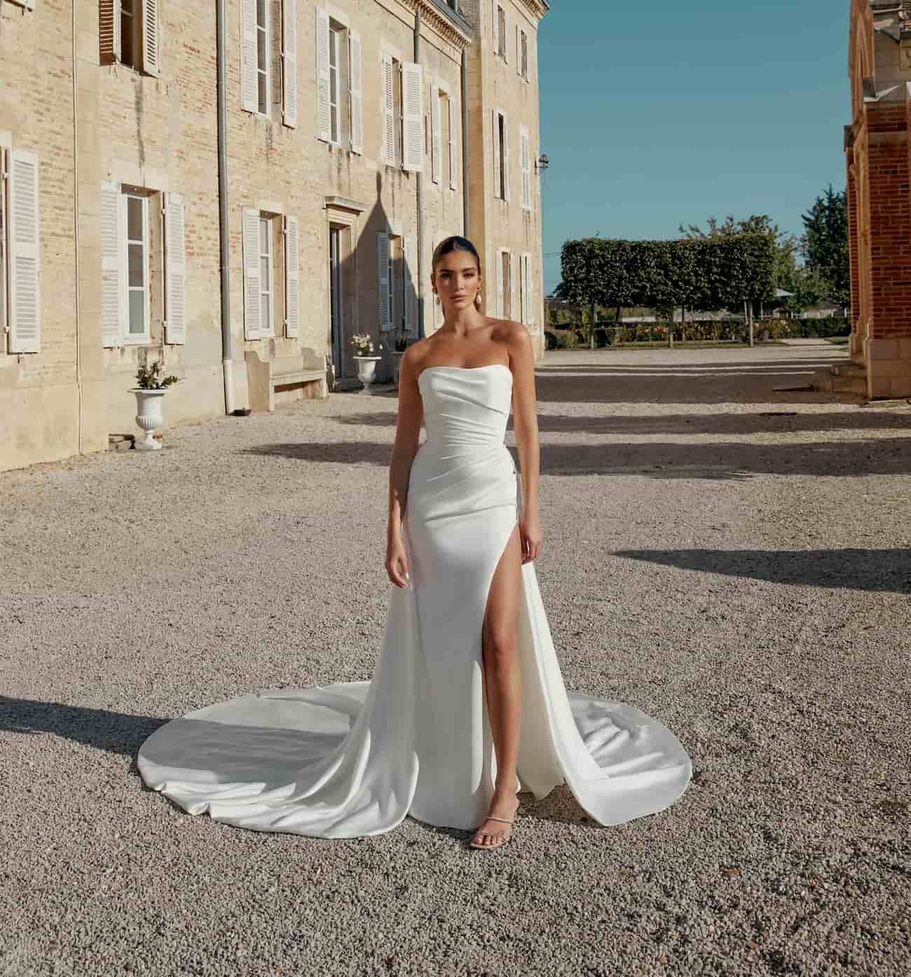 Στράπλες νυφικό από ύφασμα Charmeuse Fit and Flare με σκίσιμο στο πόδι, στενή γραμμή, ίσια λαιμόκοψη και εντυπωσιακές λεπτομέρειες. 
