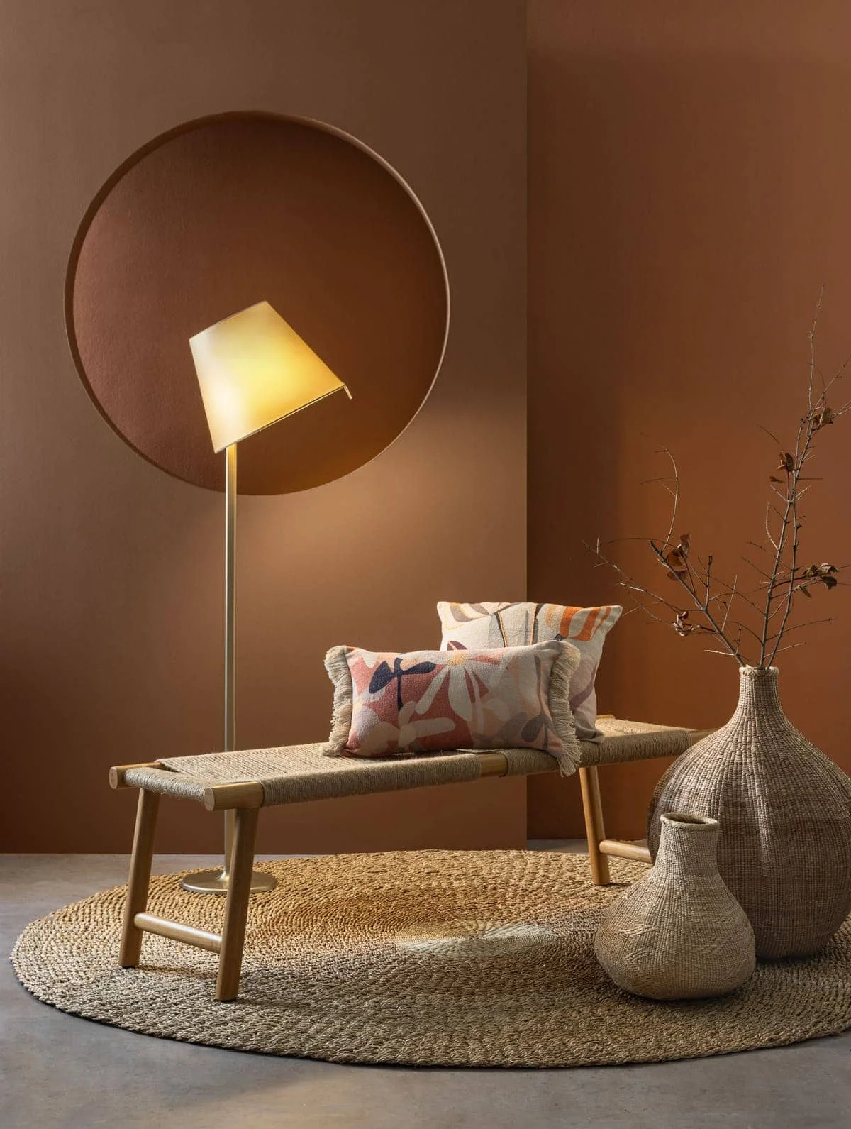 Βench «Boho», από ξύλο δρυός και φυσικό κορδόνι, Homad. Διακοσμητικά μαξιλάρια «Elma Multi», σε διάσταση 30x50, 19 €, και «Lona», σε διάσταση 45x45, 24 €, Nef-Nef Homeware. Φωτιστικό δαπέδου «Melampo-Bronze Ecru», του Adrien Gardère για την εταιρεία Artemide, Artemide Hellas. Ψάθινα βάζα «Tribe Natural», της εταιρείας Affari of Sweden, 110 € και 400 €, και στρογγυλό χαλί «The Mekong River 200», της εταιρείας Bazar Bizar, 594,40 €, όλα Interni.