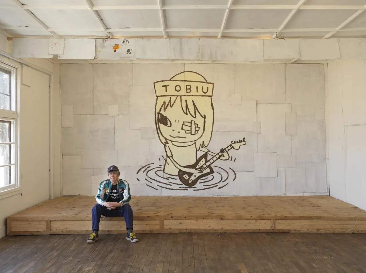 Ο Yoshitomo Nara μπροστά από το TOBIU, 2019, δωρεά του καλιτέχνη το TWO x TWO for AIDS and Art auction, 2021. Patched corrugated board mounted on wood. Image credit: © Yoshitomo Nara, courtesy Yoshitomo Nara Foundation. Photo: Ryoichi Kawajiri. Courtesy of the artist, Blum & Poe and Pace Gallery.